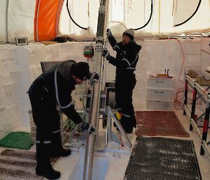 Two men inside a large tent with an ice core drill