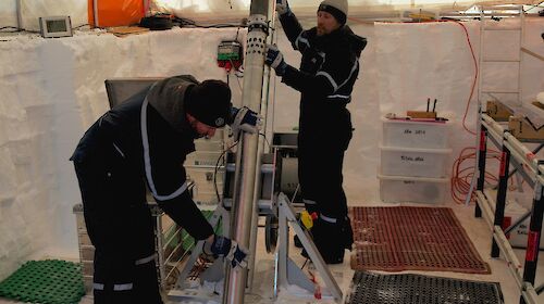 Two men inside a large tent with an ice core drill