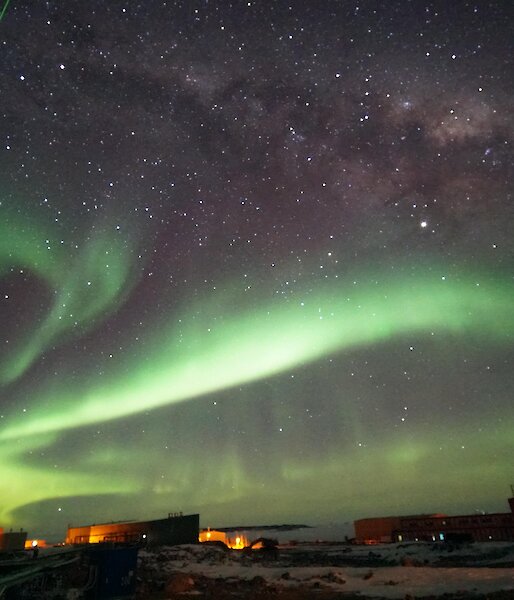 A green laser probes high-altitude clouds above Davis research station, in a night sky of auroras and stars.