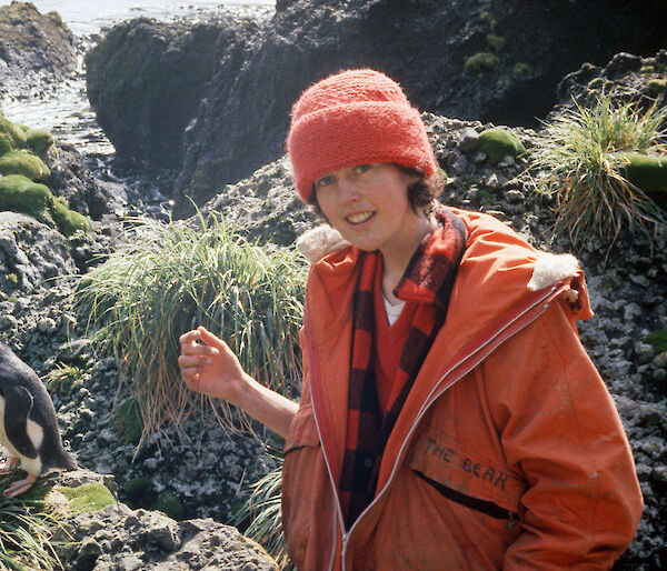 Dana Bergstrom during her first visit to Macquarie Island as a Masters student in 1983, standing beside a rocky outcrop with a penguin.