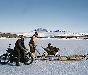 Men with motorcycle and sledge pose on the fast ice with mountain in distance behind