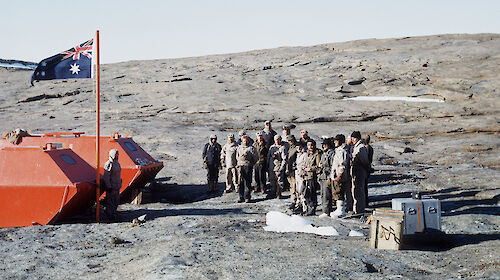 men stand to attention in front of flag on rocky coast