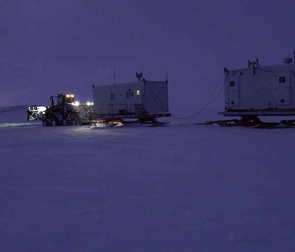 A tractor towing two shipping containers on sleds.