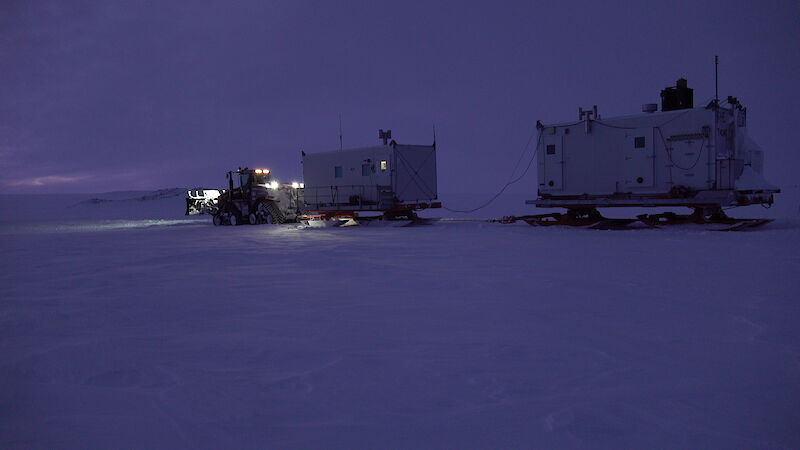 A tractor towing two shipping containers on sleds.