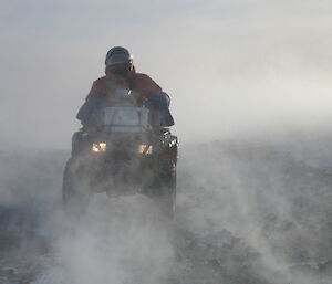 Expeditioner riding a quad bike in blowing snow.