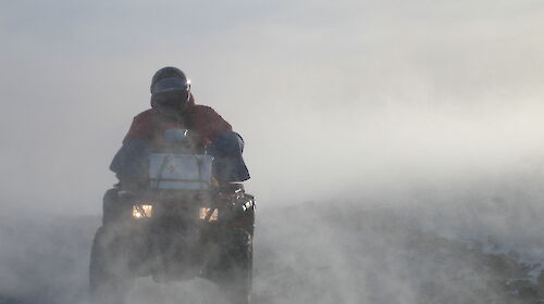 Expeditioner riding a quad bike in blowing snow.