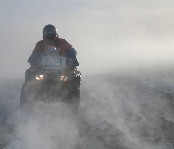 Expeditioner riding a quad bike in blowing snow.