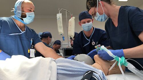 three people in an operating theatre with a mannequin
