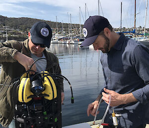 Two men preparing a piece of technical equipment next to water