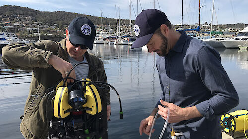 Two men preparing a piece of technical equipment next to water