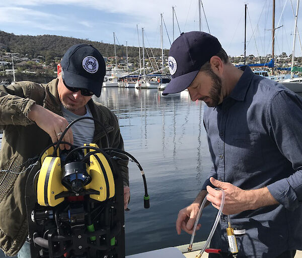 Two men preparing a piece of technical equipment next to water