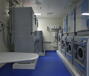 A laundry with washing machines, driers and ironing board.