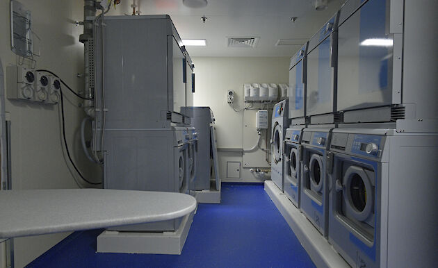 A laundry with washing machines, driers and ironing board.