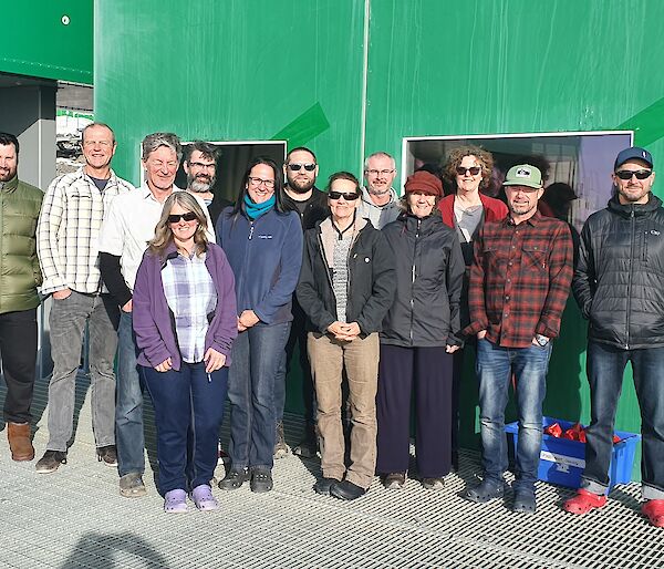 Photo of men and women standing in front of a green building