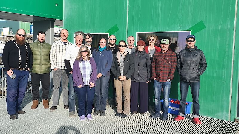 Photo of men and women standing in front of a green building