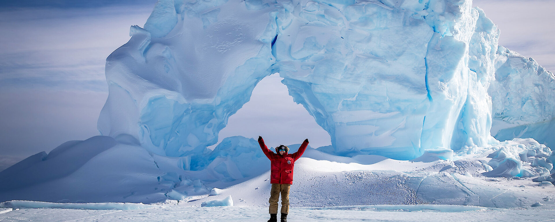 Female antarctic expedition mechanic stands in front of an iceberg