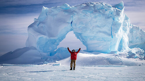 Female antarctic expedition mechanic stands in front of an iceberg
