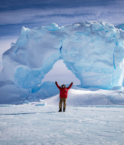 Female antarctic expedition mechanic stands in front of an iceberg