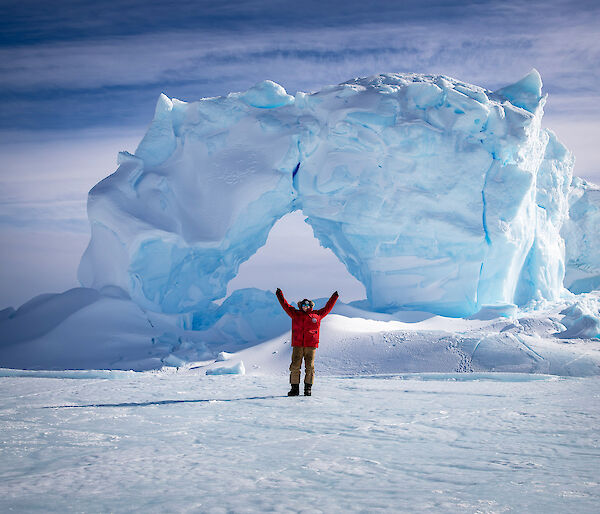 Female antarctic expedition mechanic stands in front of an iceberg