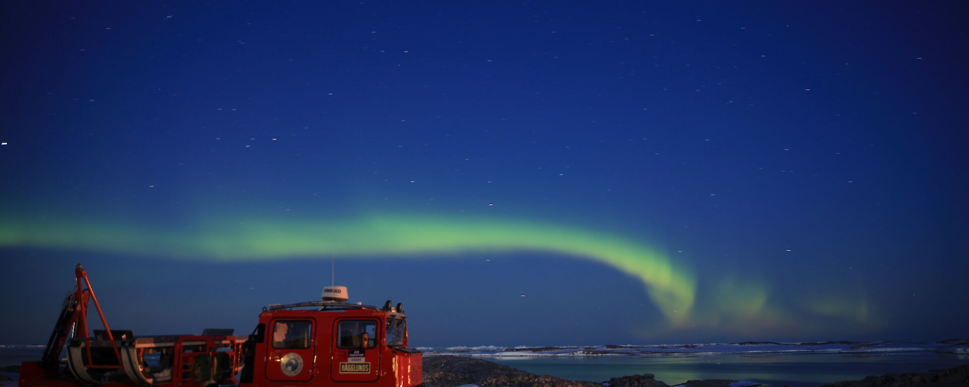 A green Aurora Australis over the bay with the Red Hagg in the foreground