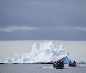 Two small boat moving in front of an iceberg