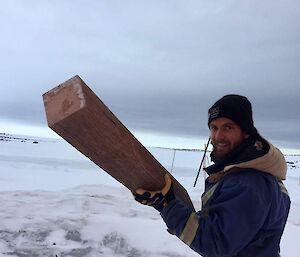 Aaron carrying a large peice of wood standing on snow and ice