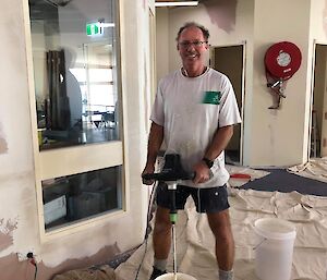 Alan mixing paint in the Red Shed in shorts and a T-shirt