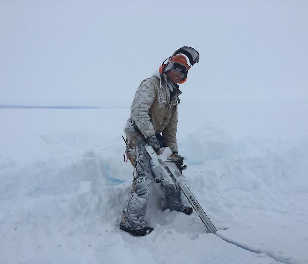 Conrad cutting into the ice with a chainsaw