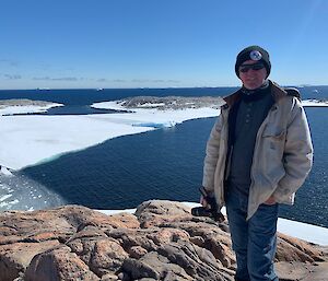 Jason standing on Reeves Hill with the ocean with islands and ice in the background