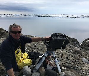 Jason working on a camera on rocks with the bay and snow covered islands in the background