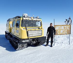 Sam standing at the Antarctic Circle sign with the yellow Hagg