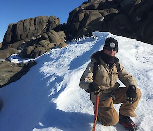 Conrad kneeling on the snow with rocks and penguins in the background