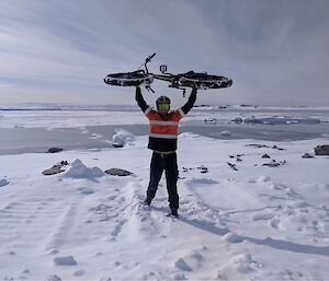 Aaron lifting a fat bike whilst standing on the snow with icebergs in the background