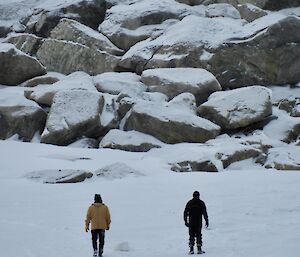 The backs of David and Alan as they return from a wharf walk with large bolders in front of them