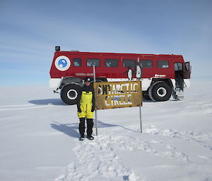 Jason standing at the Antarctic circle sign with the Terrabus in the background