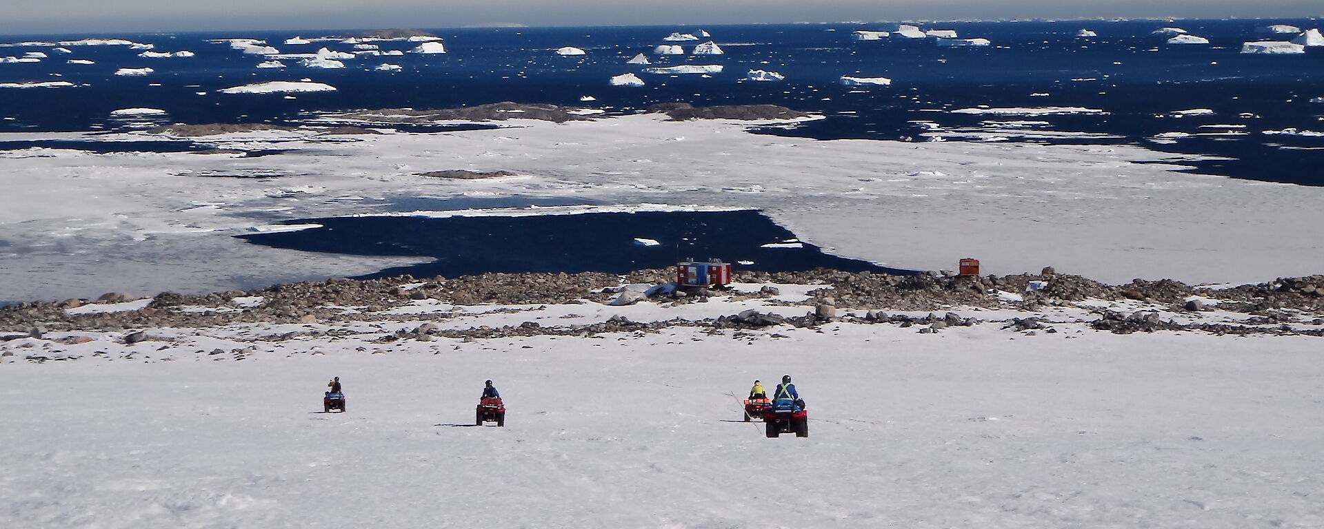 Four quads and riders heading down the hill toards Jack’s Hut with the ocean and icebergs in the background