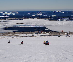 Four quads and riders heading down the hill toards Jack’s Hut with the ocean and icebergs in the background