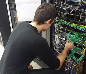 Sam kneeling in front of a cabint working on cables