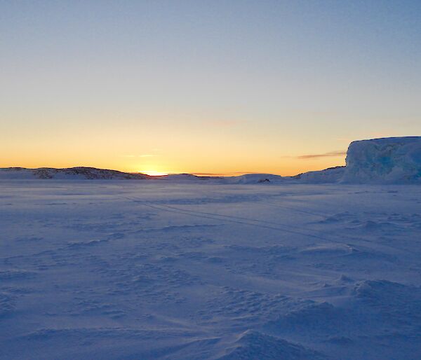 Sunrise on the ice with an island and sea ice cliff in the background