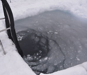 A swimming hole with a laddr and ice floating on top