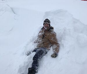 Scott laying in the snow with the top of the Red Shed in the background