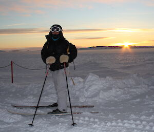 Tanya on skiis at the wharf with snow all around and the sun just above the horizon