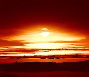 The sun above the horizon with a bright orange glow over the icebergs