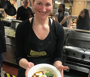 Jords with a bowl of ramen noodle soup in the kitchen with a couple of her helpers in the background