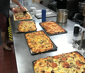 Several pizzas on the kitchen table being cut by Aaron with Tanya and Garvin looking on