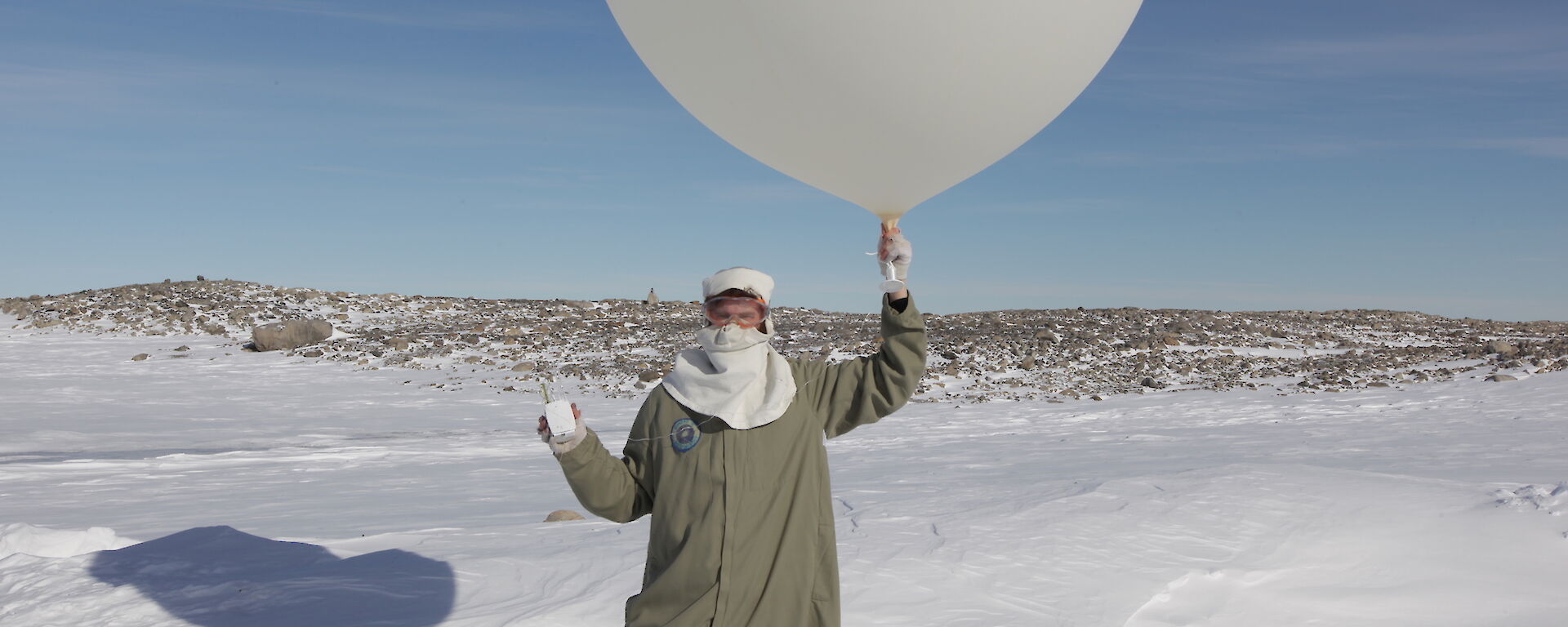 Craig holding a Weather Balloon and Radiosonde just before release standing in the snow and with rocks in the background