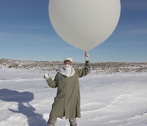 Craig holding a Weather Balloon and Radiosonde just before release standing in the snow and with rocks in the background
