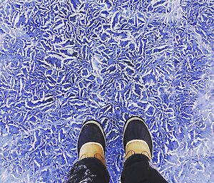 A photo into the ice and its patterns with two boots and the bottom of the trousers shown