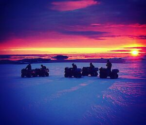 Five quads and riders on the ice with a sunset in the bacground and throughout the sky
