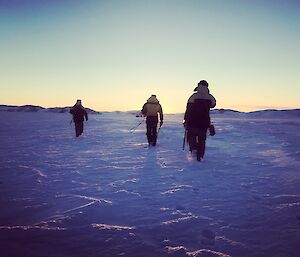 Three expeditioners walking across the ice and into the sun